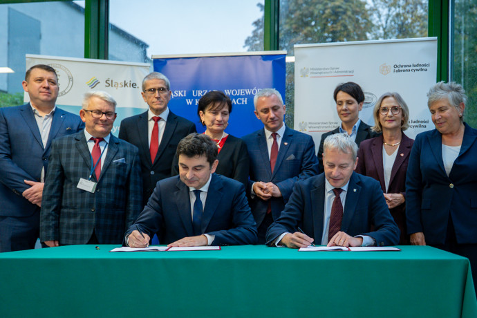 Wojewoda i Marszałek przy stole podpisują umowę. W tle zaproszeni goście.
